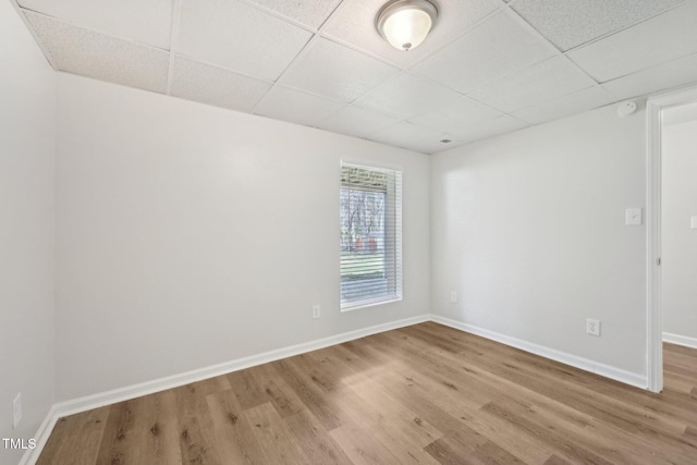 empty room featuring baseboards, a drop ceiling, and wood finished floors