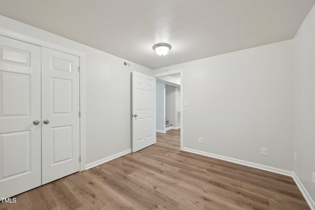 unfurnished bedroom featuring visible vents, baseboards, a closet, and wood finished floors