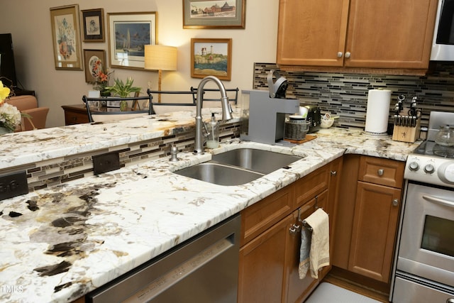 kitchen featuring backsplash, a sink, light stone countertops, brown cabinets, and stainless steel appliances