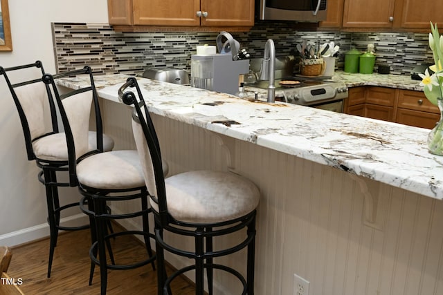 kitchen featuring backsplash, wood finished floors, a kitchen breakfast bar, appliances with stainless steel finishes, and brown cabinetry