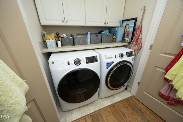 laundry room featuring washing machine and clothes dryer, cabinet space, and wood finished floors