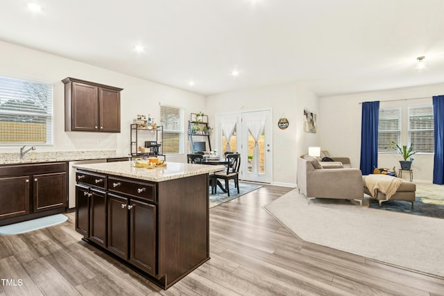 kitchen with dark brown cabinetry, a sink, a center island, open floor plan, and light wood-style floors