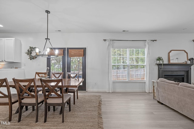 dining area featuring light wood-style flooring, visible vents, baseboards, a glass covered fireplace, and an inviting chandelier