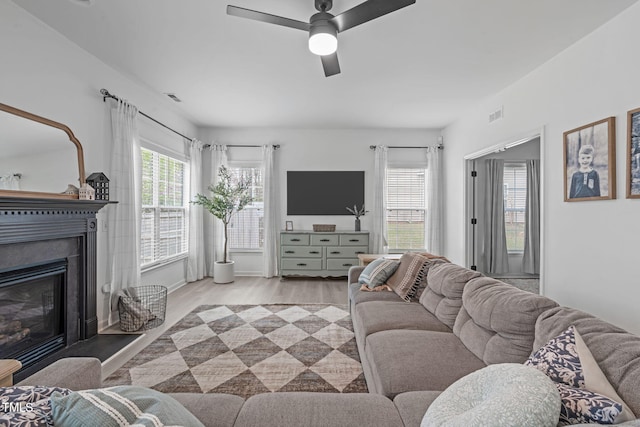 living room featuring ceiling fan, a glass covered fireplace, wood finished floors, and visible vents