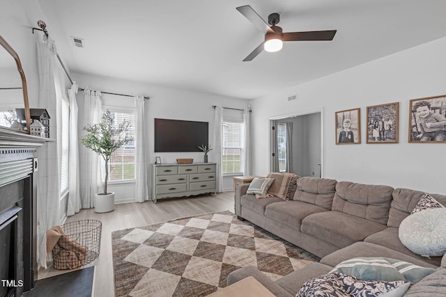 living room with ceiling fan, wood finished floors, visible vents, and a fireplace