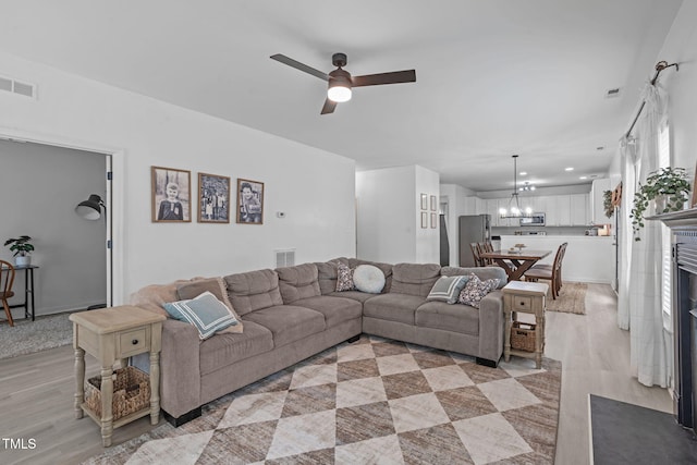 living room featuring light wood-type flooring, visible vents, and ceiling fan with notable chandelier