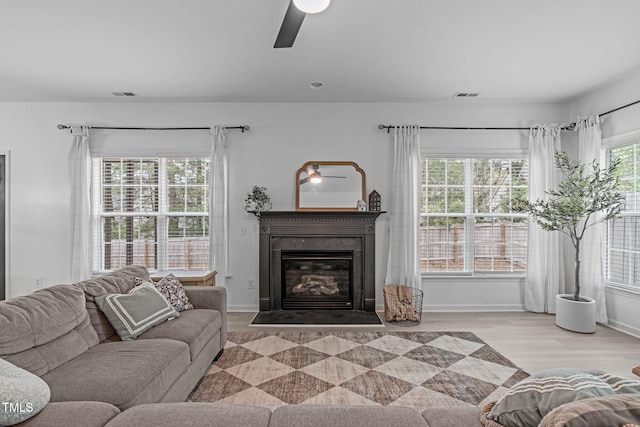 living room with wood finished floors, a glass covered fireplace, a ceiling fan, and visible vents