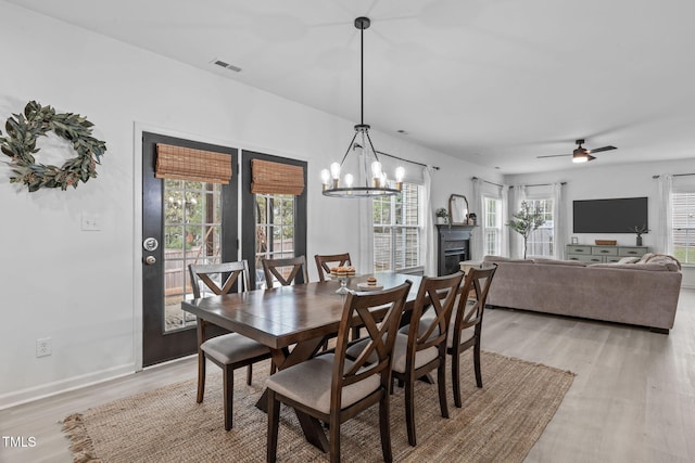 dining space featuring light wood finished floors, baseboards, visible vents, and ceiling fan with notable chandelier