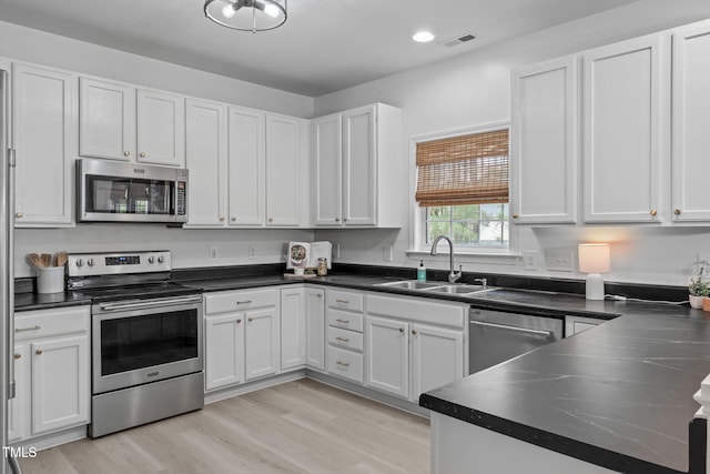kitchen featuring white cabinets, stainless steel appliances, visible vents, a sink, and light wood-type flooring