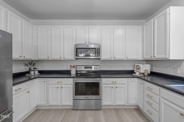 kitchen with white cabinets, light wood-style floors, dark countertops, and appliances with stainless steel finishes