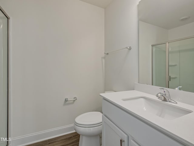 full bathroom featuring wood finished floors, vanity, baseboards, toilet, and a shower with door