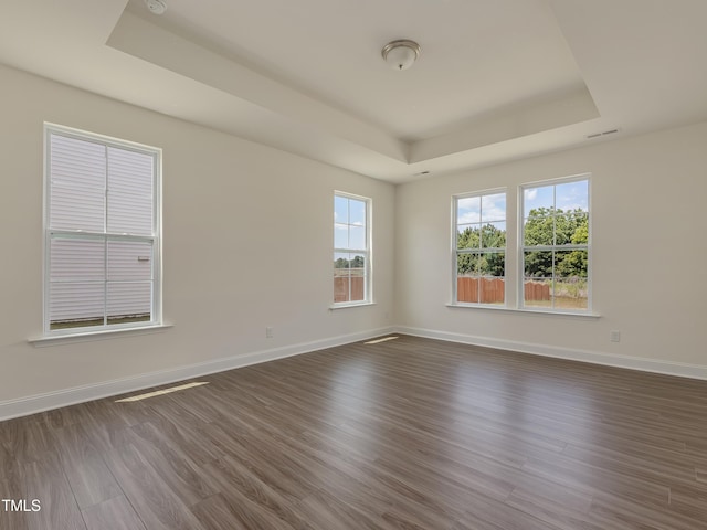 spare room featuring a raised ceiling, baseboards, dark wood finished floors, and visible vents