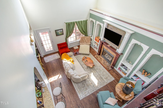living area with a glass covered fireplace, wood finished floors, a high ceiling, and arched walkways