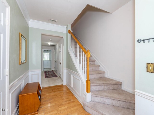 stairs with crown molding, wood finished floors, wainscoting, and a decorative wall