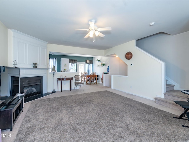 living room with light colored carpet, a ceiling fan, stairs, and a fireplace