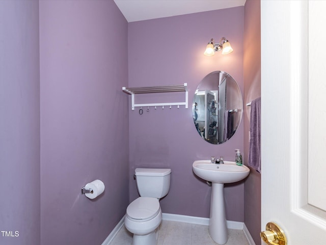 half bathroom with toilet, baseboards, tile patterned flooring, and a sink
