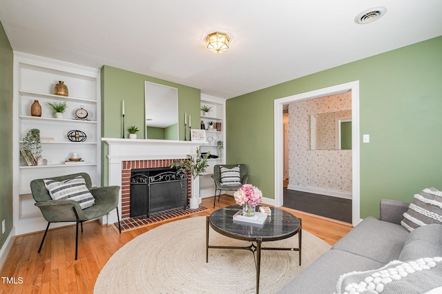 living room with wood finished floors, a brick fireplace, visible vents, baseboards, and wallpapered walls