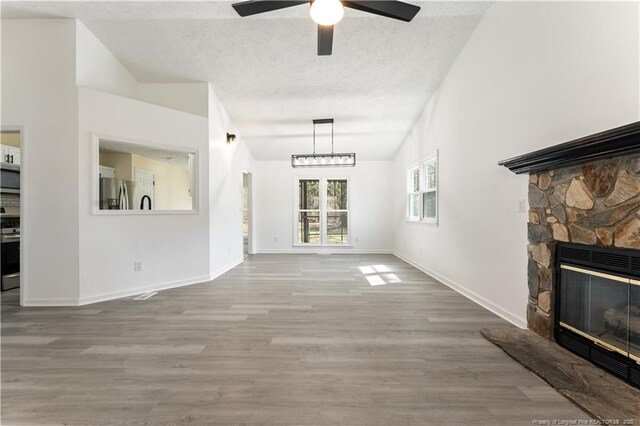 131 Windsor Ln, Raeford, NC 28376 - unfurnished living room featuring ceiling fan, a textured ceiling, wood finished floors, a stone fireplace, and baseboards