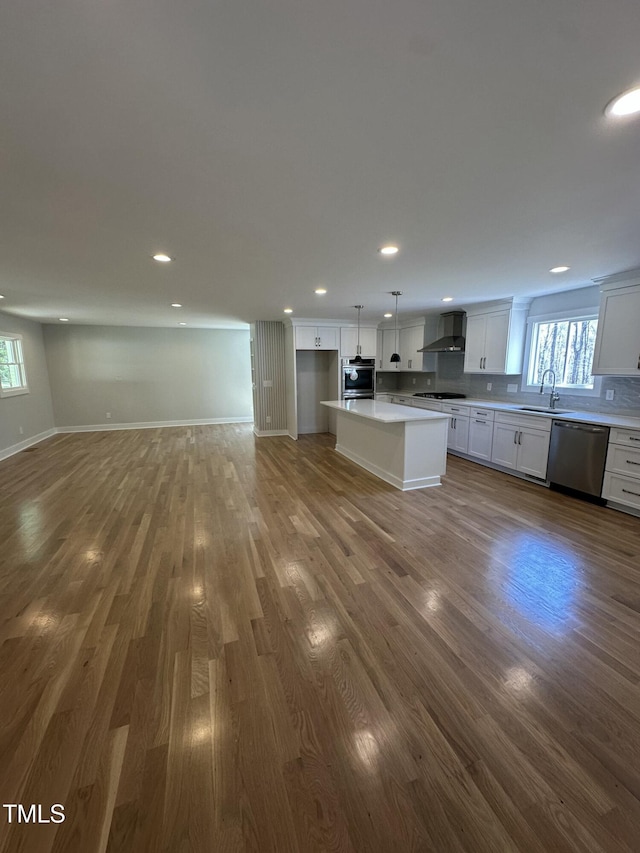 kitchen featuring open floor plan, plenty of natural light, a sink, wall chimney range hood, and appliances with stainless steel finishes