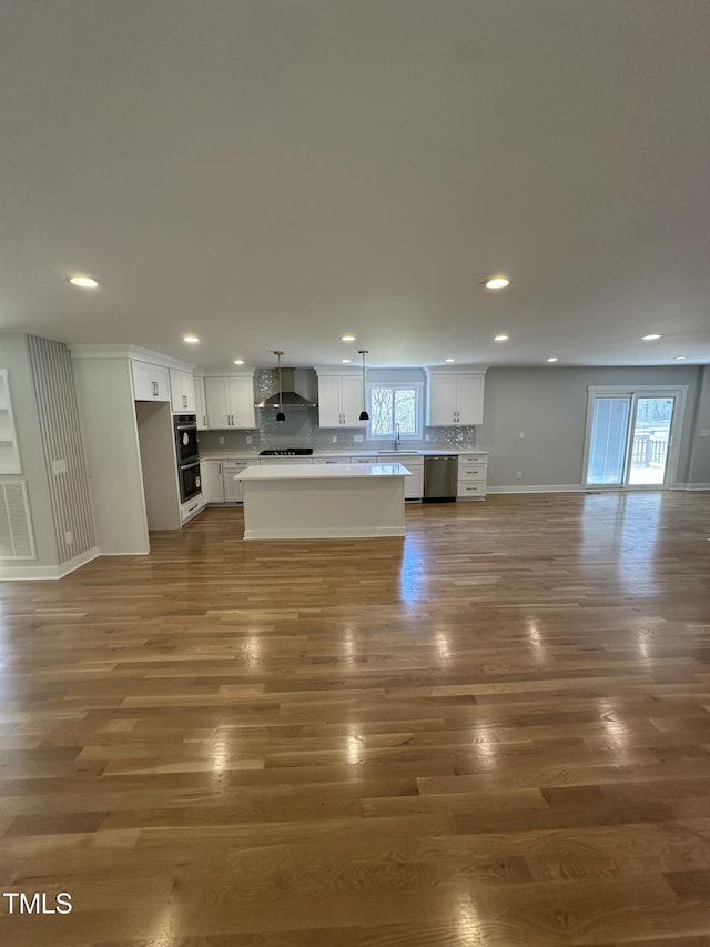 kitchen featuring dark wood-style flooring, stainless steel dishwasher, open floor plan, wall chimney range hood, and backsplash