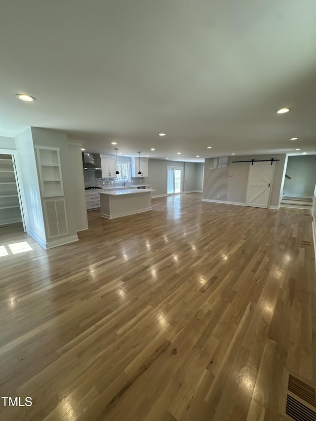 unfurnished living room featuring recessed lighting, baseboards, a barn door, visible vents, and wood finished floors