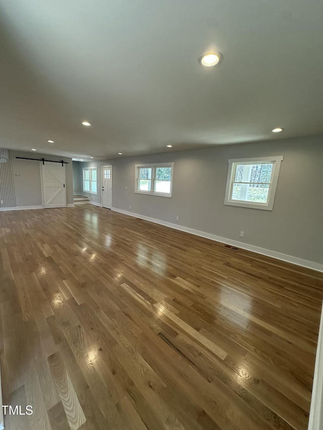 unfurnished living room with baseboards, a barn door, wood finished floors, and recessed lighting