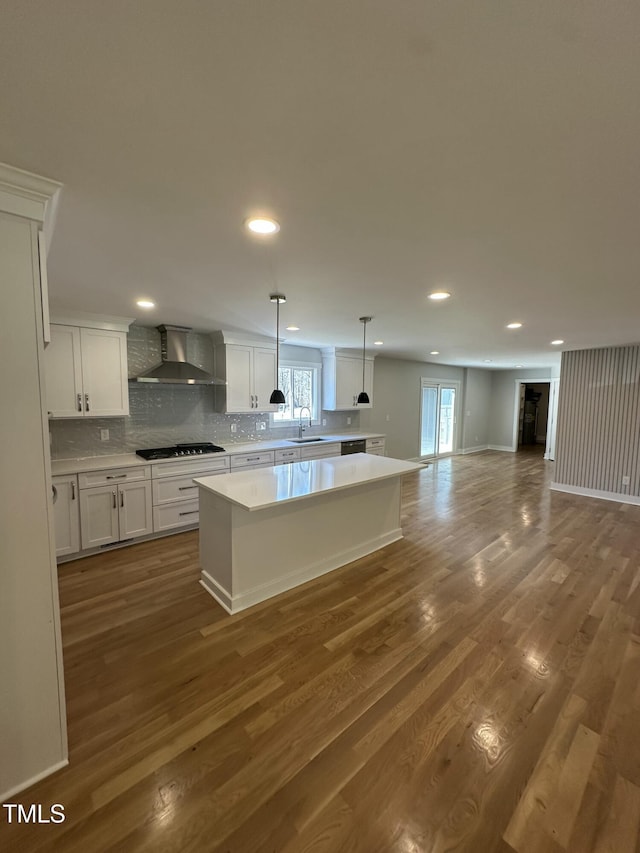 kitchen with a sink, wall chimney exhaust hood, gas stovetop, a center island, and a healthy amount of sunlight