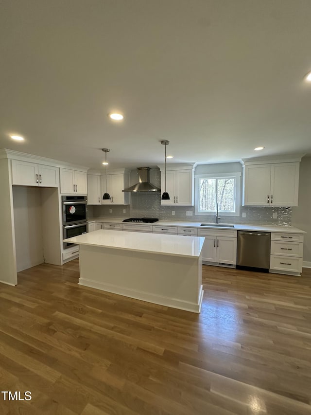 kitchen featuring a sink, a kitchen island, wall chimney exhaust hood, stainless steel appliances, and white cabinets
