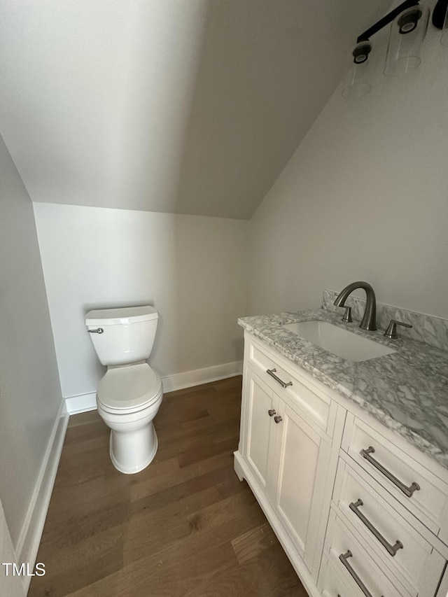 bathroom with vanity, lofted ceiling, toilet, baseboards, and wood finished floors
