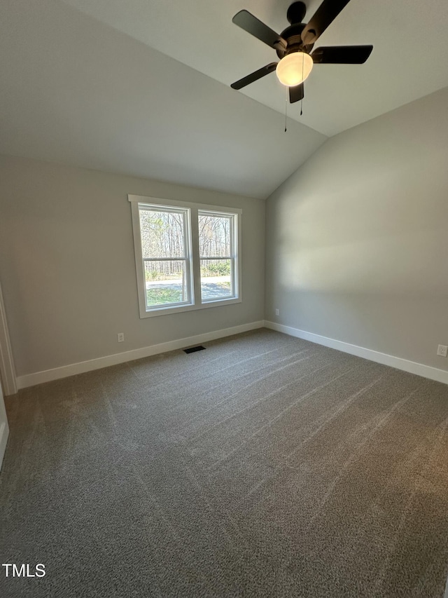 spare room with lofted ceiling, baseboards, dark carpet, visible vents, and a ceiling fan