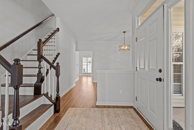 foyer with baseboards, a notable chandelier, wood finished floors, and stairway
