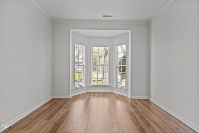 spare room with baseboards, visible vents, crown molding, and wood finished floors