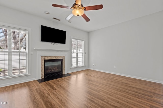 unfurnished living room with baseboards, visible vents, a ceiling fan, a fireplace, and wood finished floors