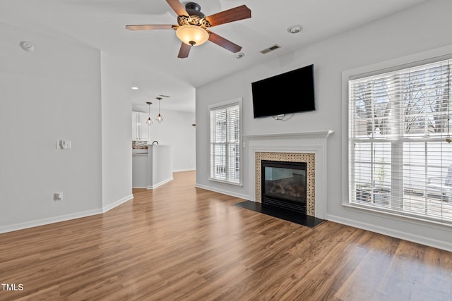 unfurnished living room featuring a tile fireplace, wood finished floors, baseboards, visible vents, and ceiling fan