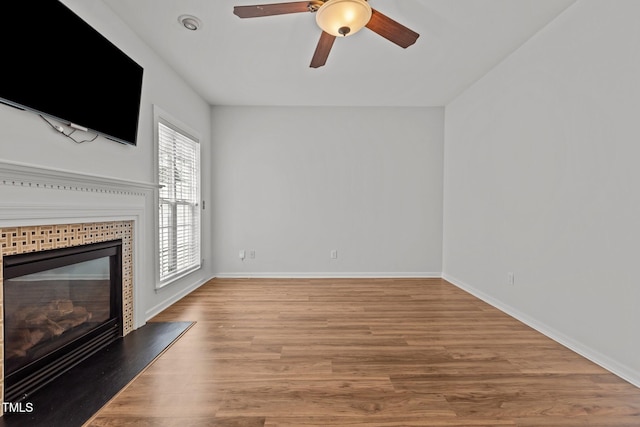 unfurnished living room featuring baseboards, a fireplace, wood finished floors, and ceiling fan