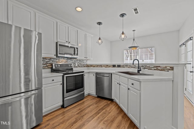 kitchen with visible vents, light wood-style flooring, a peninsula, appliances with stainless steel finishes, and a sink