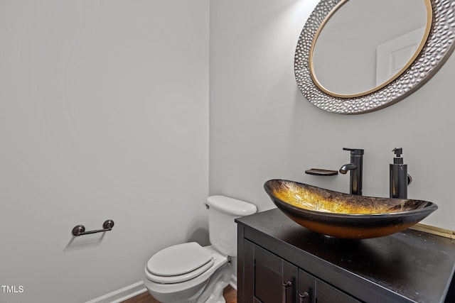 half bathroom featuring toilet, vanity, and baseboards
