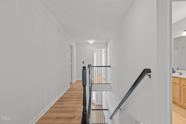 hall with baseboards, light wood-type flooring, an upstairs landing, and a sink