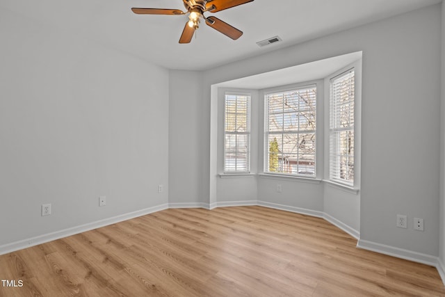spare room featuring baseboards, visible vents, light wood-style floors, and a ceiling fan