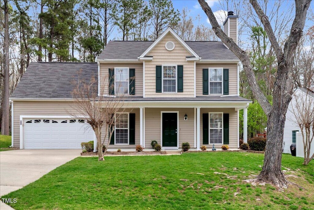 view of front facade with an attached garage, a chimney, a front yard, driveway, and a porch