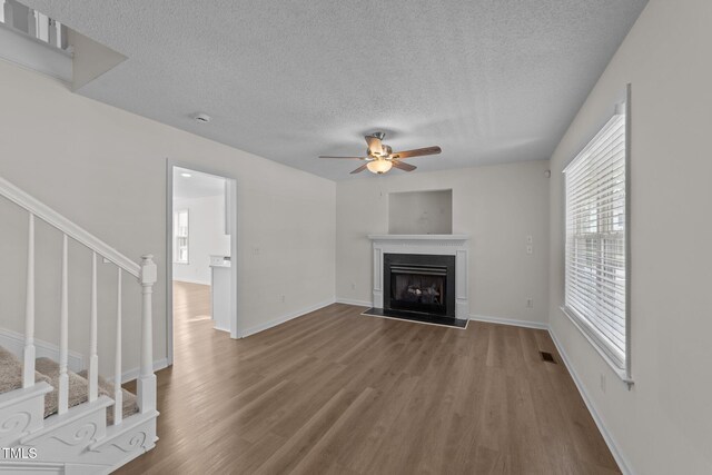 unfurnished living room with a ceiling fan, a textured ceiling, wood finished floors, and a wealth of natural light