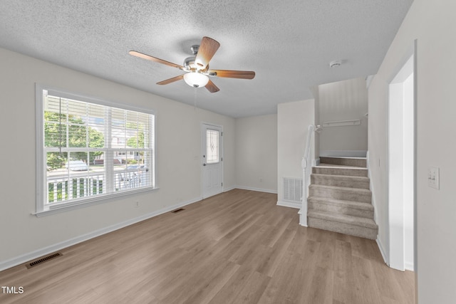 unfurnished living room with a ceiling fan, stairs, light wood-style flooring, and visible vents
