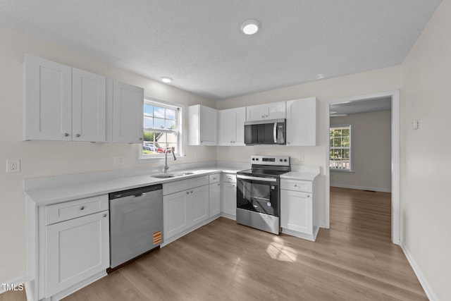 kitchen with white cabinets, a sink, light countertops, a textured ceiling, and stainless steel appliances