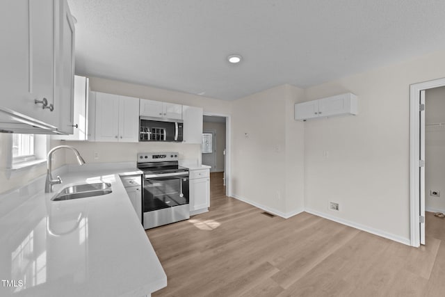 kitchen with light countertops, white cabinets, a sink, light wood-style flooring, and appliances with stainless steel finishes