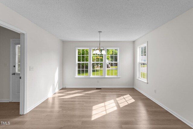 unfurnished dining area featuring wood finished floors, baseboards, a textured ceiling, and a notable chandelier