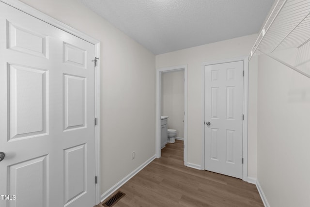 hallway with baseboards, a textured ceiling, wood finished floors, and visible vents
