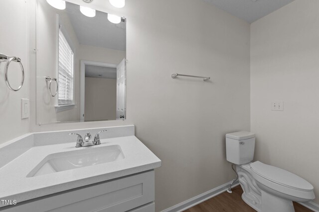 bathroom with toilet, baseboards, wood finished floors, and vanity