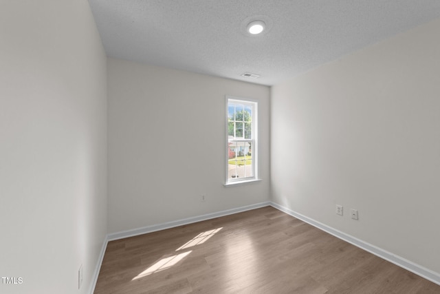 unfurnished room featuring baseboards, a textured ceiling, visible vents, and wood finished floors