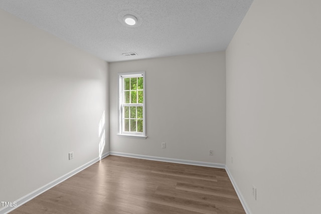 spare room with baseboards, a textured ceiling, visible vents, and wood finished floors