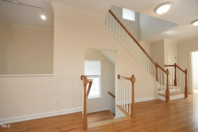 stairway featuring baseboards, wood finished floors, rail lighting, and ornamental molding